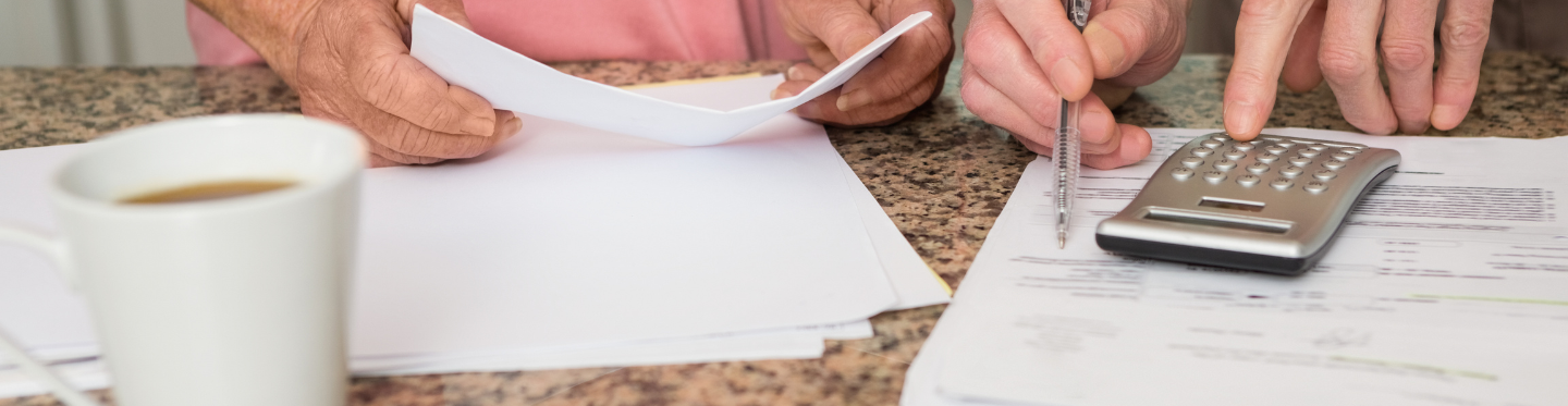 Two people looking at monthly bill, all that is shown is their torsos and hands and paper and a calculator and a cup of coffee.